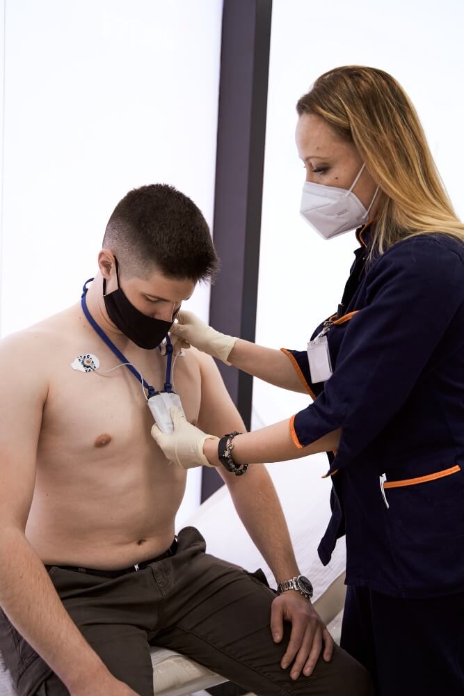 The nurse is fitting the 24-hour Holter monitor on the patient.